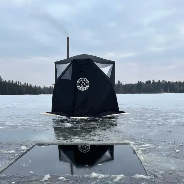 North Shore Sauna tent set up on a frozen lake, with steam rising from the chimney.